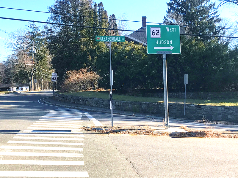 Figure 15 - View across Gleasondale Road (Route 62) of Southeast Intersection Corner. Image shows crosswalk passing to the left of a median to a tall curb and narrow sidewalk made of pavement. Figure 15 - View across Gleasondale Road (Route 62) of Southeast Intersection Corner. Image shows crosswalk passing to the left of a median to a tall curb and narrow sidewalk made of pavement.